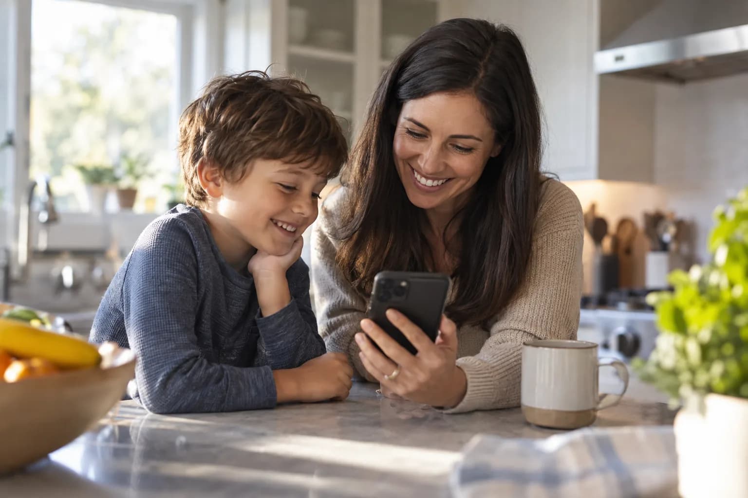 Parent and child looking at a chore chart app together on a phone at the kitchen counter